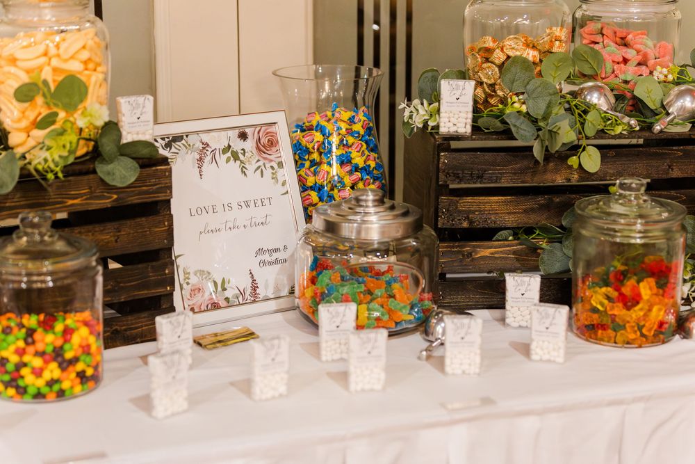 Colorful candy buffet display with glass jars filled with various sweets and labeled name cards at a dessert table.