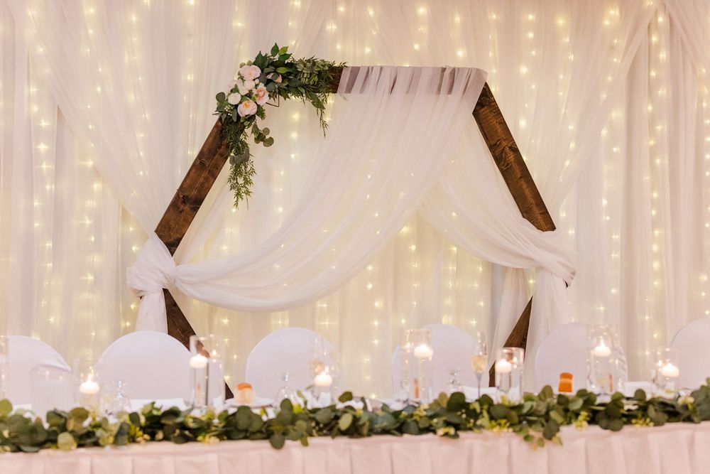 A romantic wedding venue decorated with twinkling string lights, white drapes, and floral garlands creating an ethereal atmosphere.