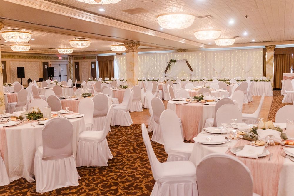 Elegant white wedding reception hall with round tables, white linens, and crystal chandeliers.
