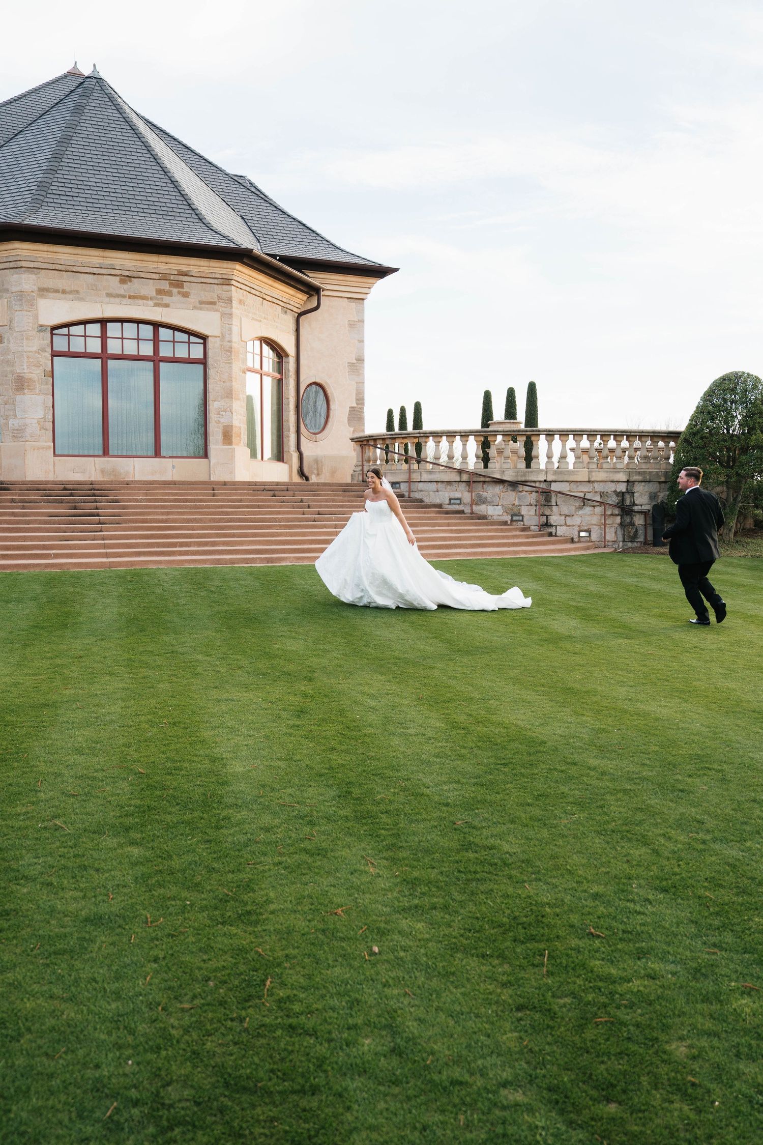 Joyful wedding party walking and laughing together on a grassy lawn during golden hour at sunset.