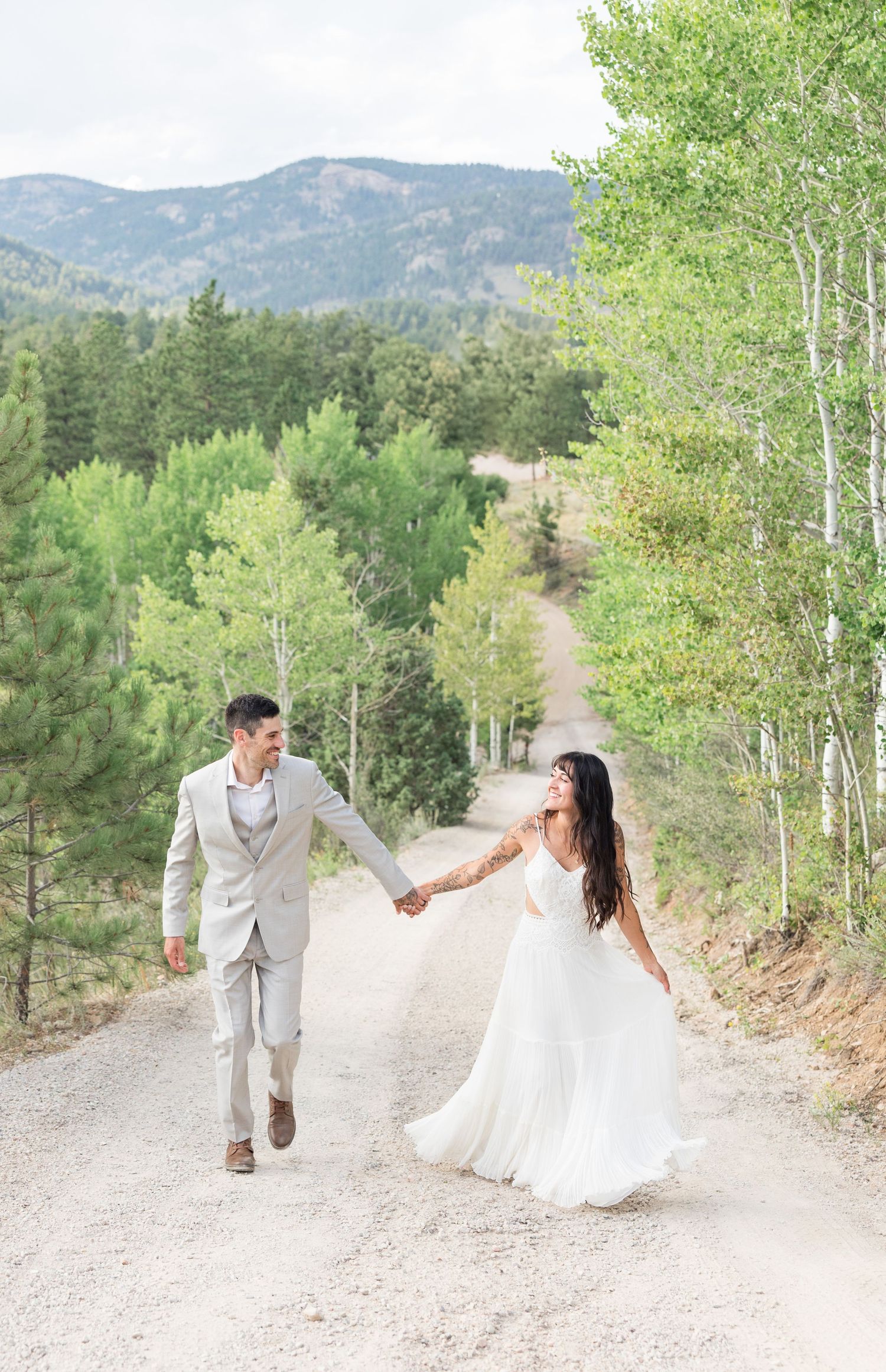 Newlywed couple walk hand in hand along a scenic mountain path surrounded by aspen trees on their wedding day.