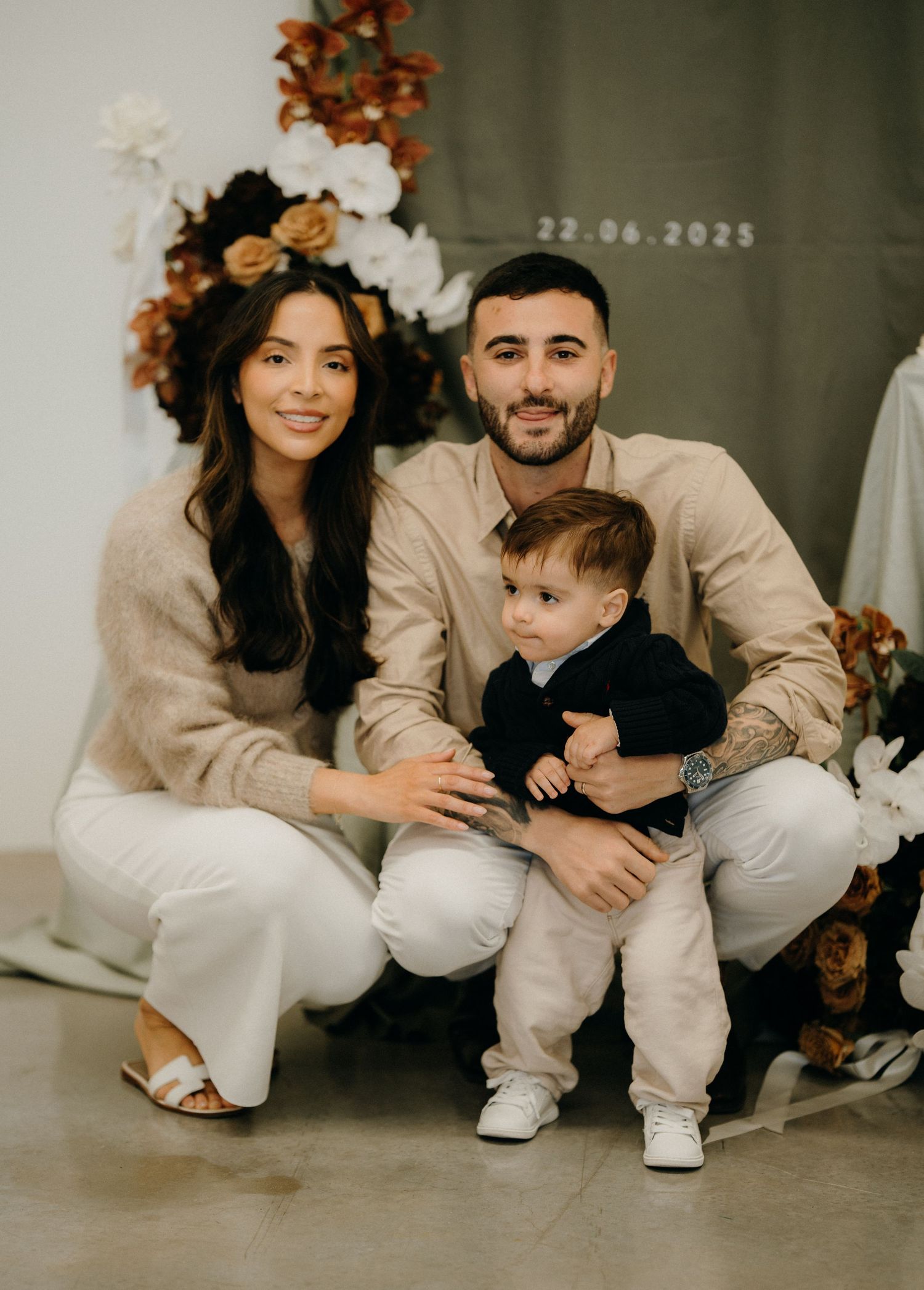 Family in matching white outfits poses together against a dark green wall with autumn-colored decorative leaves.