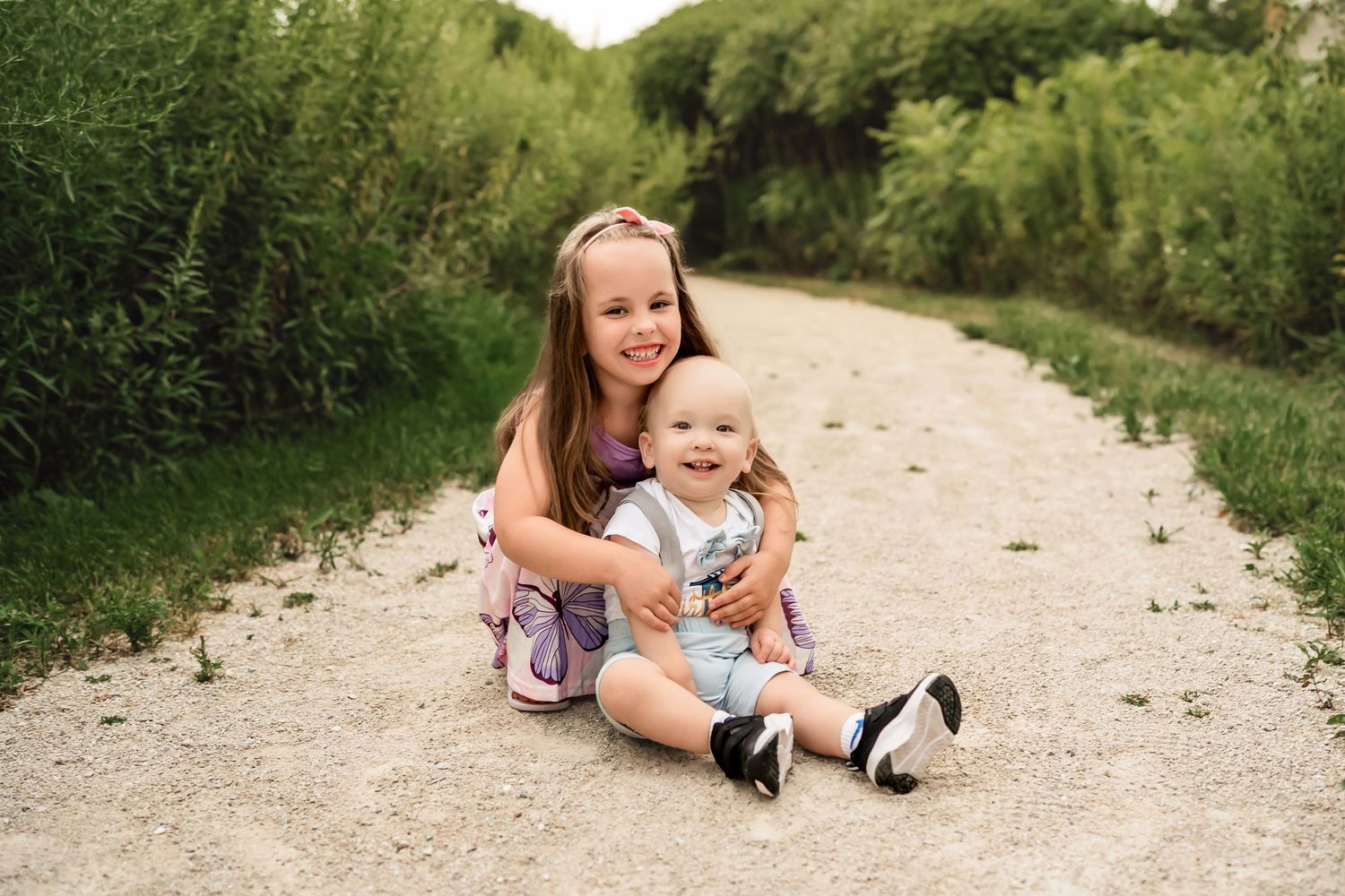 Children play and explore together on a winding dirt path through lush summer greenery and trees.