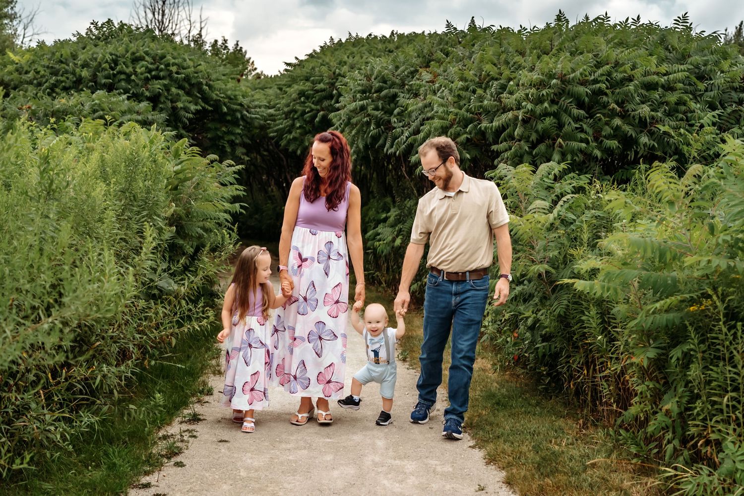 Family walking together hand in hand down a lush green nature trail surrounded by summer foliage.