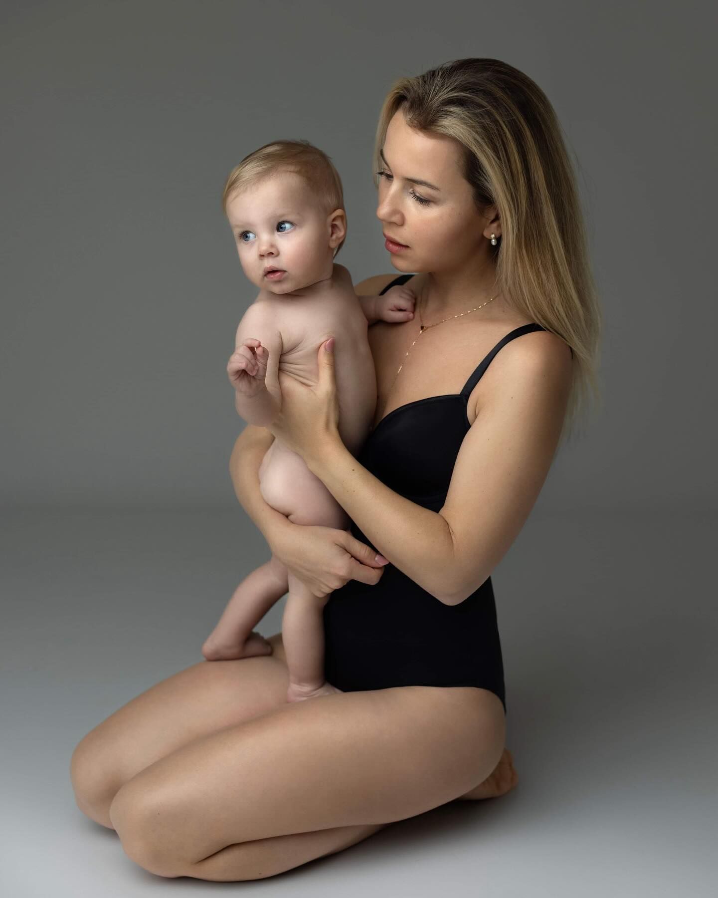 A tender moment captures varying poses of parent and infant in black leotard against neutral studio backdrop.