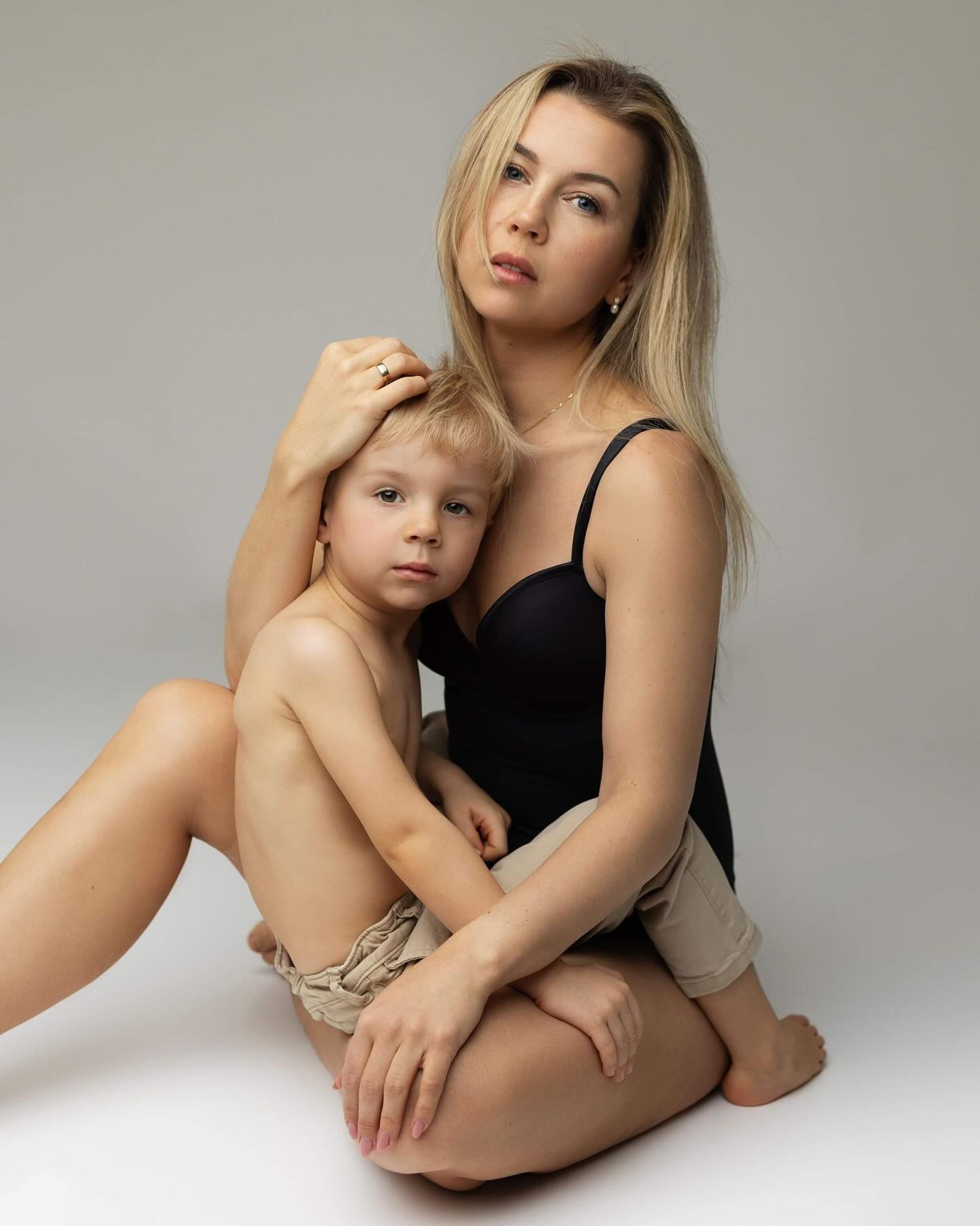 A mother and young child sharing tender moments in a minimalist portrait studio setting with white background.