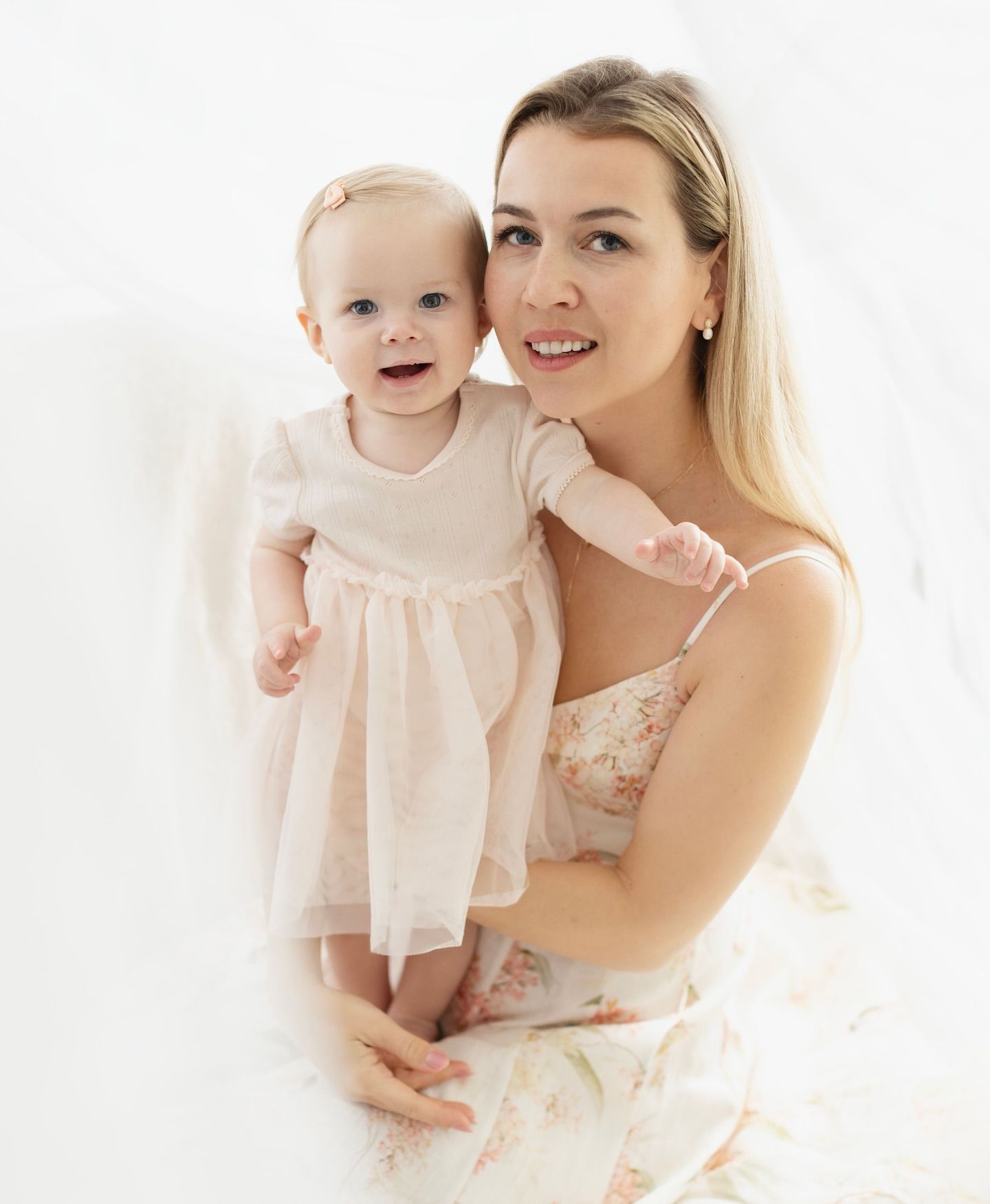 Mother and baby wearing matching white outfits pose together for a sweet family photography session.