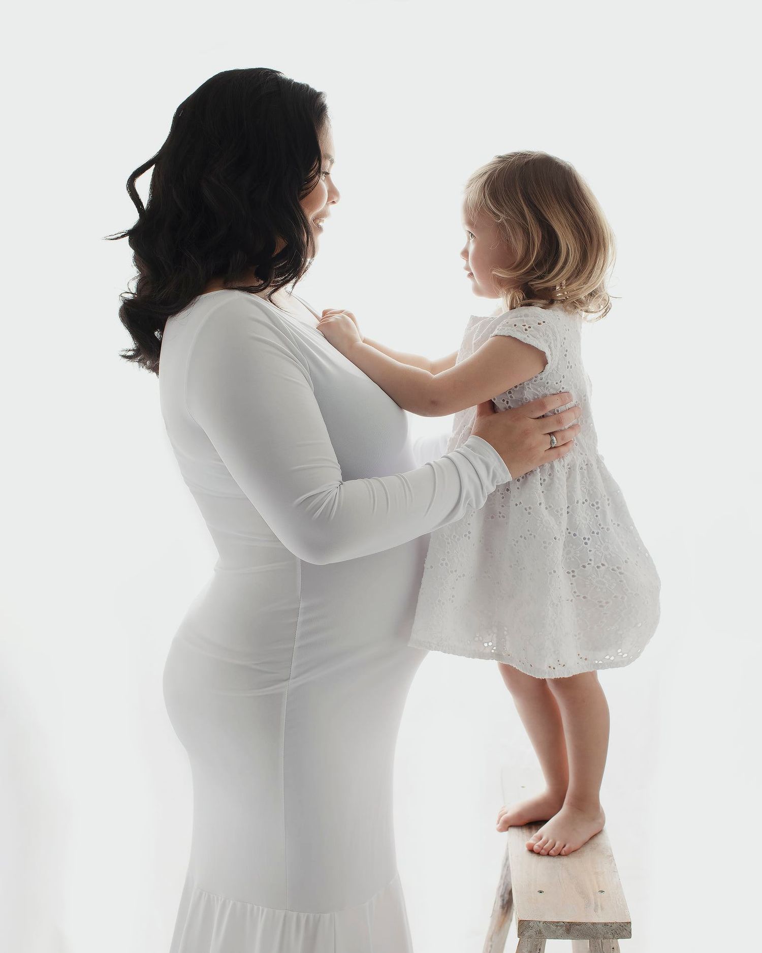 A white dress wearing woman lifts a small child in white clothing against a light background in sequential shots.