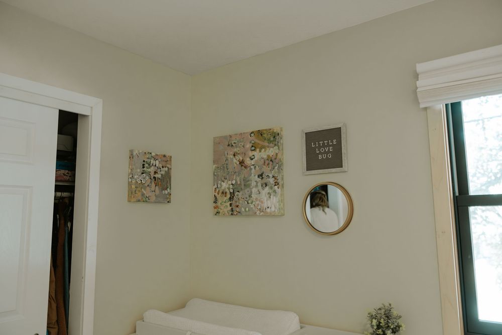 Nursery room wall decorated with abstract art prints and a round mirror.