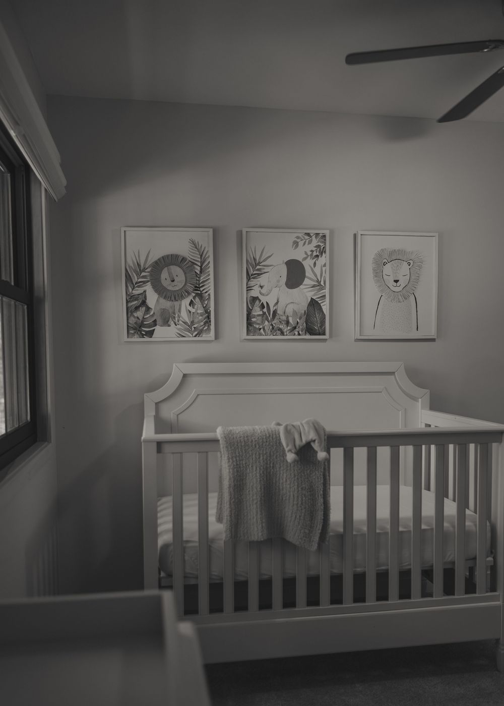 A minimalist nursery with white crib and three framed botanical and animal artwork prints on the gray wall.