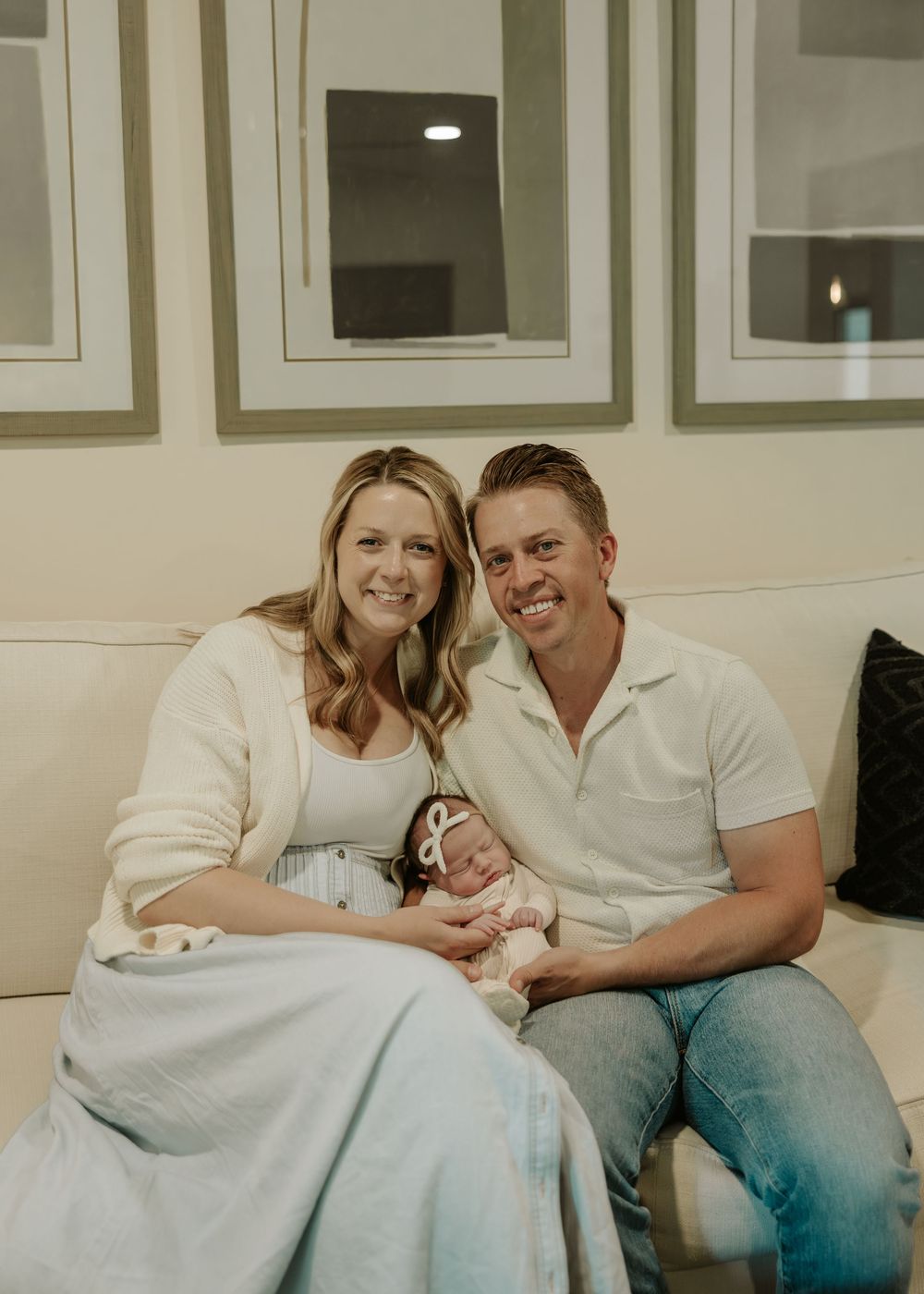 New parents snuggle with their newborn baby while relaxing on a white couch in a cozy room.