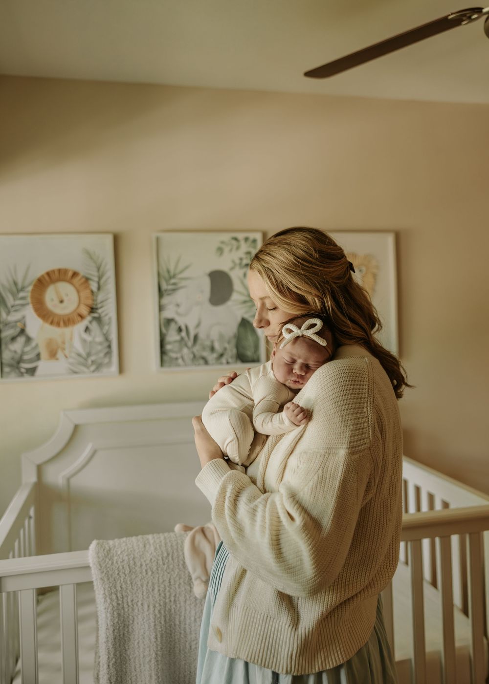 Parent holding sleeping baby in white nursery with botanical artwork on wall.