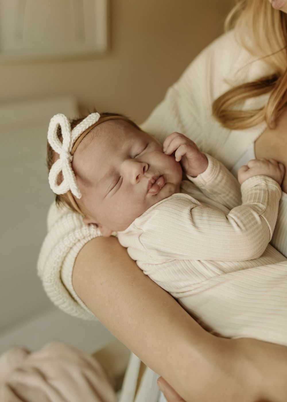Close up of peaceful sleeping newborn wearing bow headband and cream colored outfit.