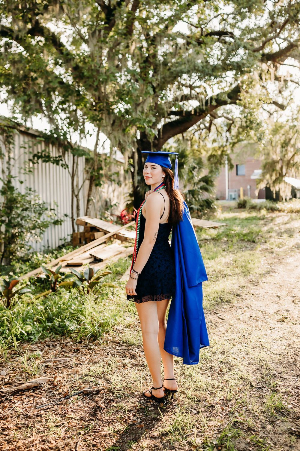 Figure in black clothing and blue cape strikes poses against a sunlit outdoor natural background.