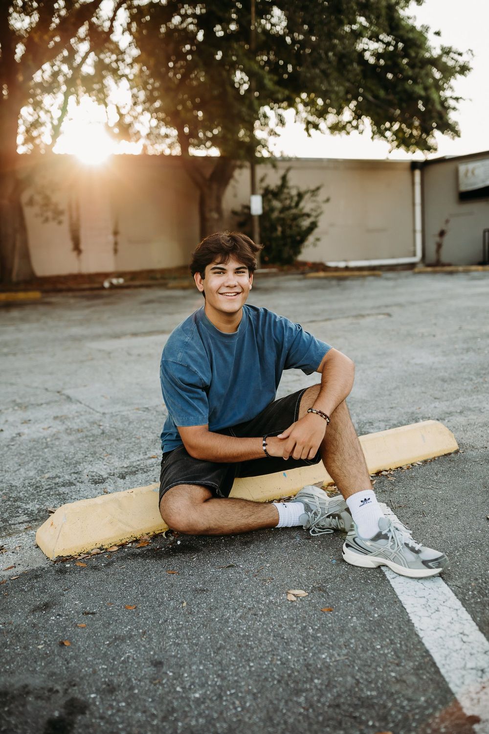 Person in blue t-shirt lying casually on pavement with sunlight creating warm evening ambiance.