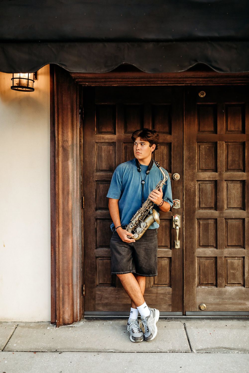 A panoramic photo sequence shows someone sitting in front of wooden doors holding a saxophone in casual attire.
