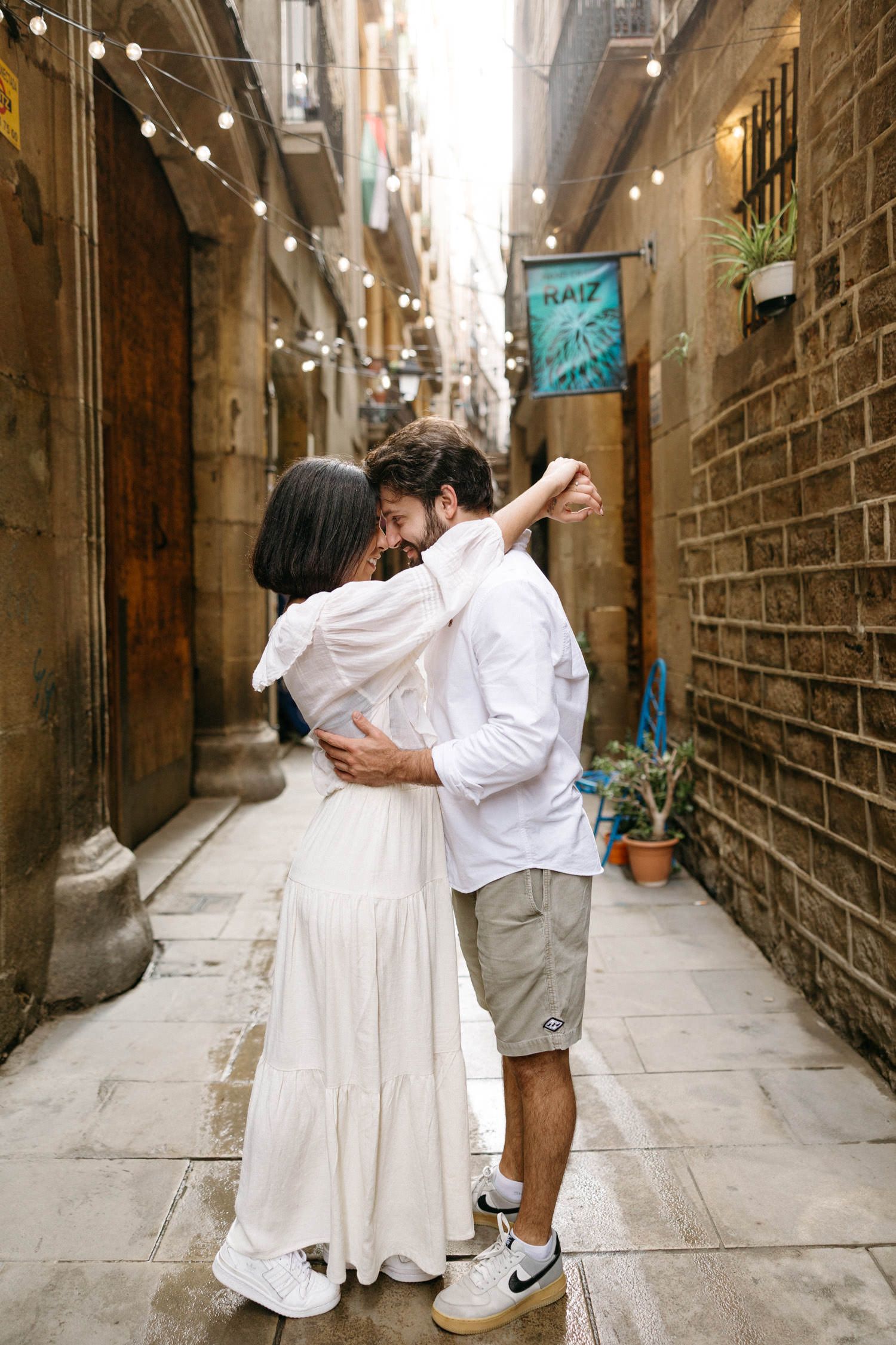 A romantic couple shares intimate moments in a narrow European alley with brick walls and string lights.