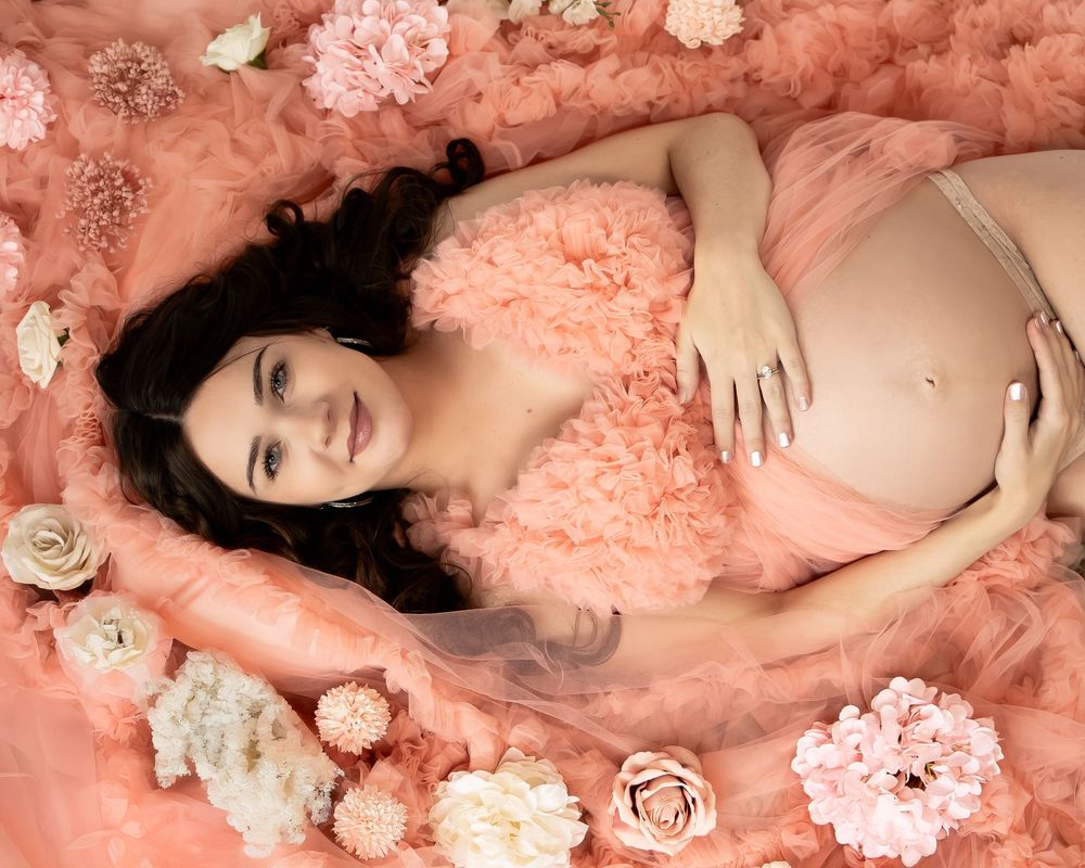 A dreamy fashion portrait series in soft coral lighting features roses, tulle fabric, and delicate white butterfly decorations.