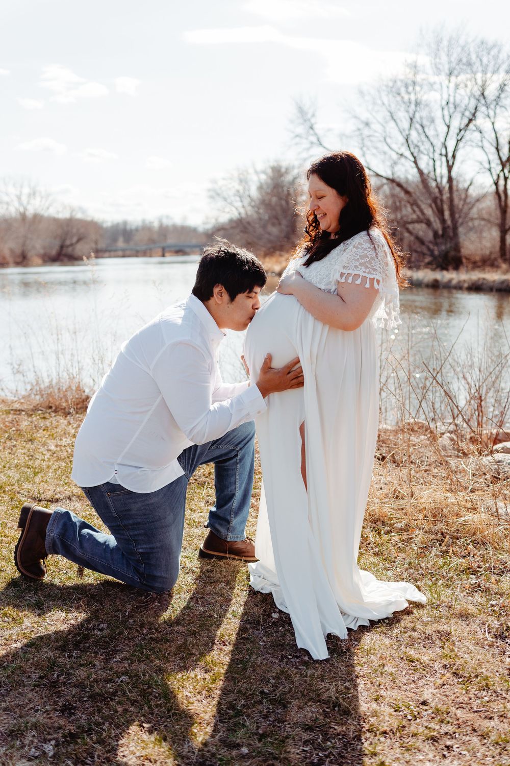 Couple sitting together outdoors by a lake in casual attire during golden hour.