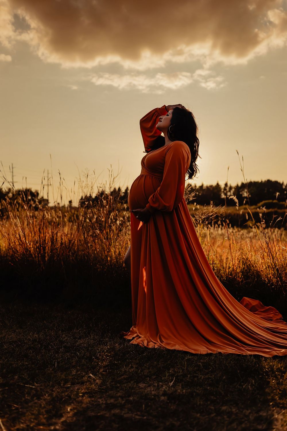 A figure in a flowing red dress stands dramatically in a golden field at sunset creating a moody silhouette.