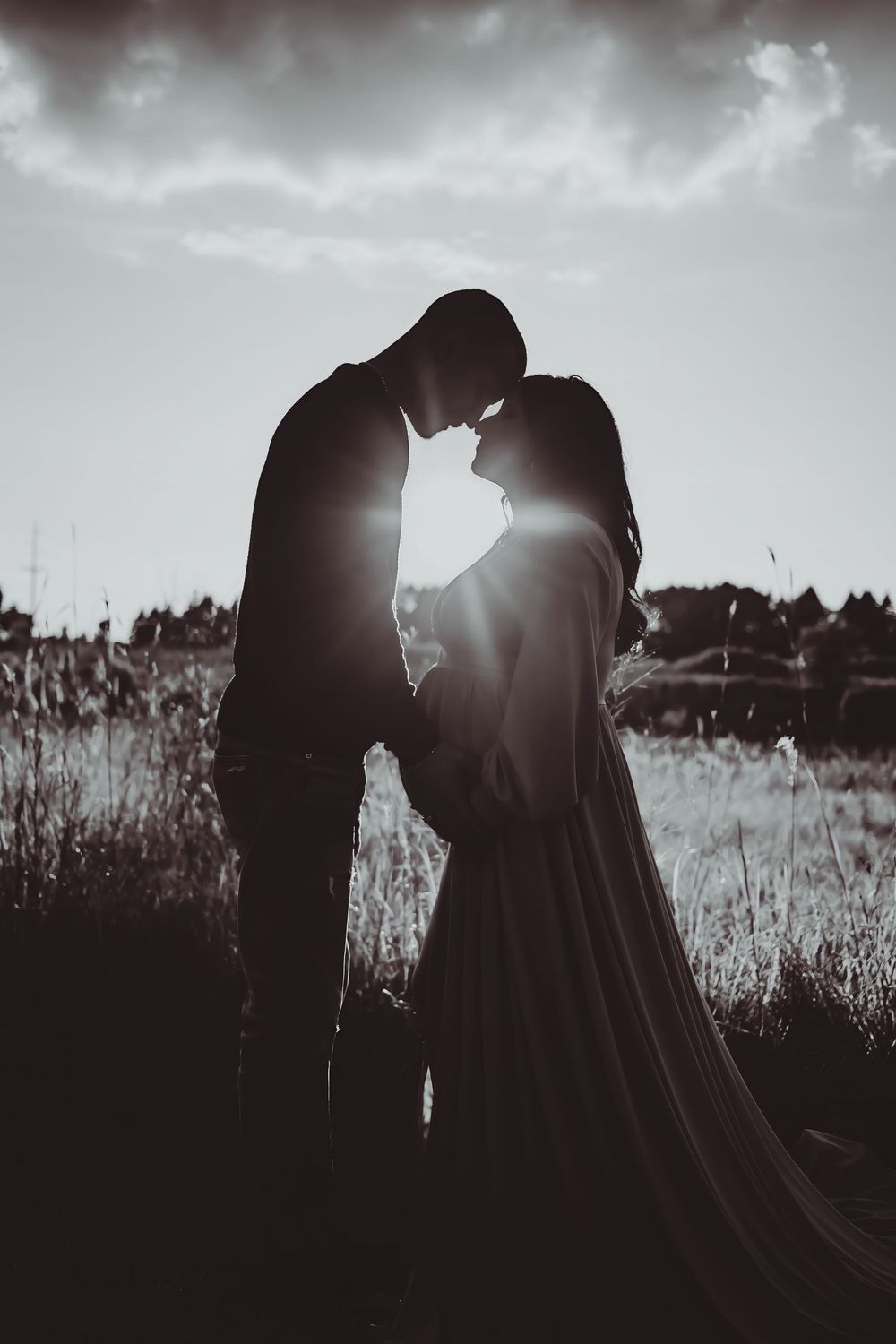 A romantic silhouette of a couple embracing in a field at sunset captured in a black and white photo sequence.