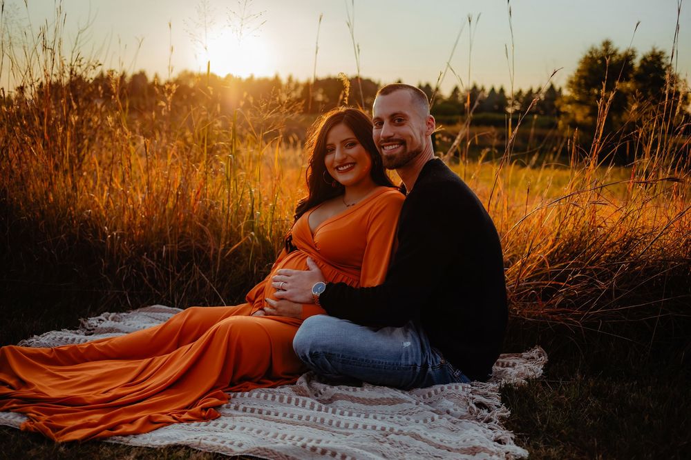 Couple poses together on a blanket in a golden field during sunset for romantic photos.