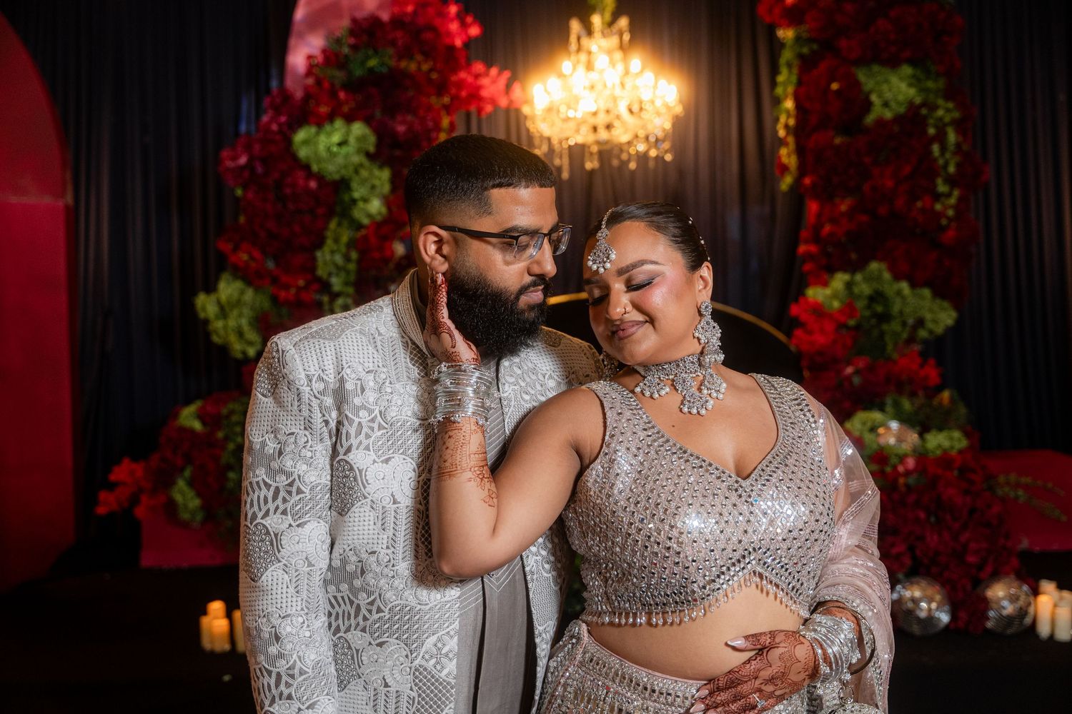 Traditional Indian wedding couple posing in formal attire against elegant room with gold mirror.