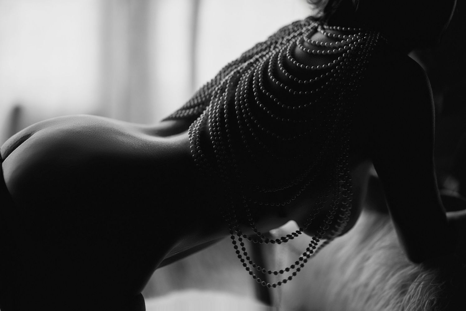 Black and white artistic photo of a woman adorned with elegant pearl body jewelry draped across her back.