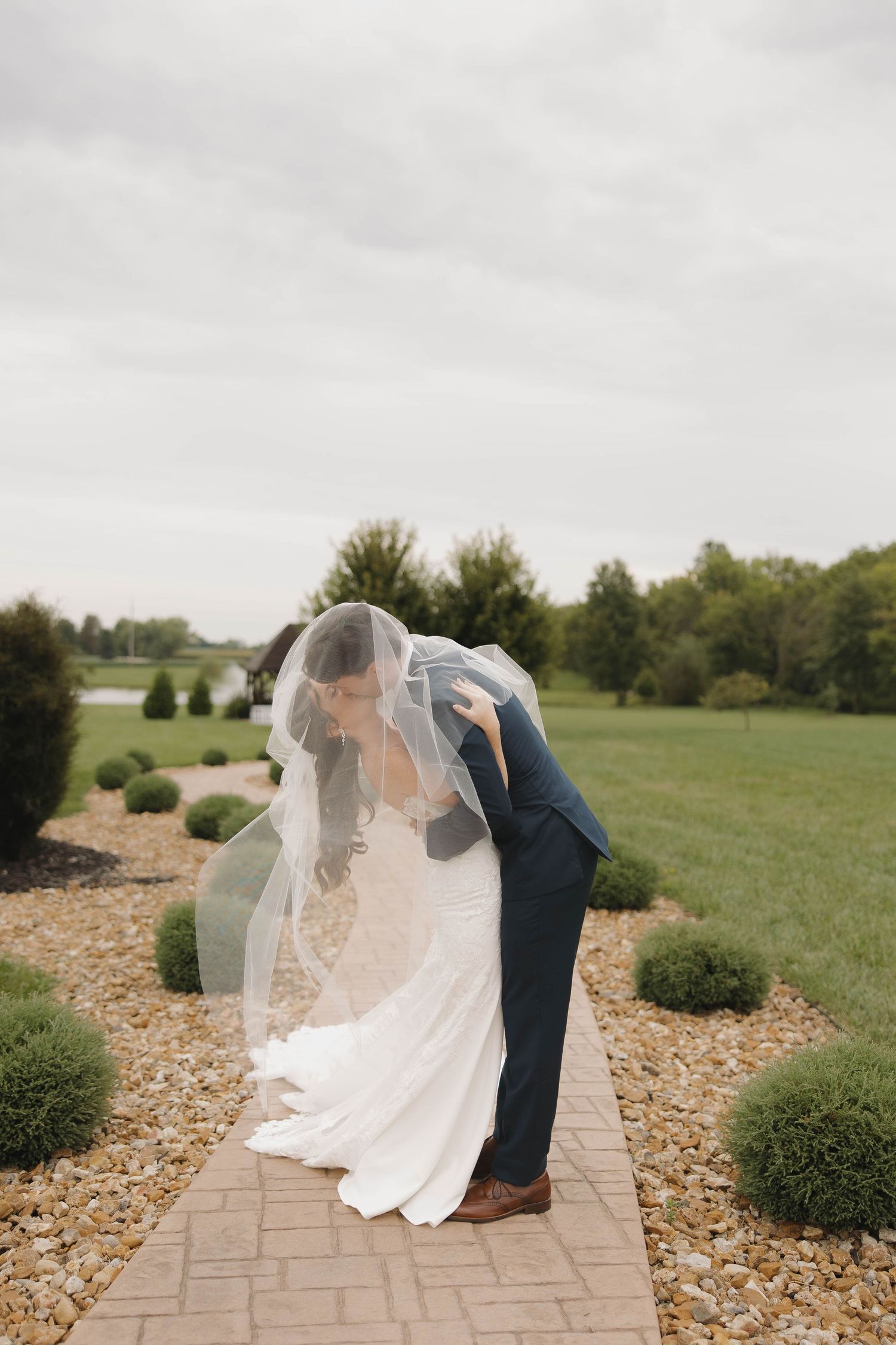 A couple in wedding attire embraces on a decorative stone pathway with greenery.
