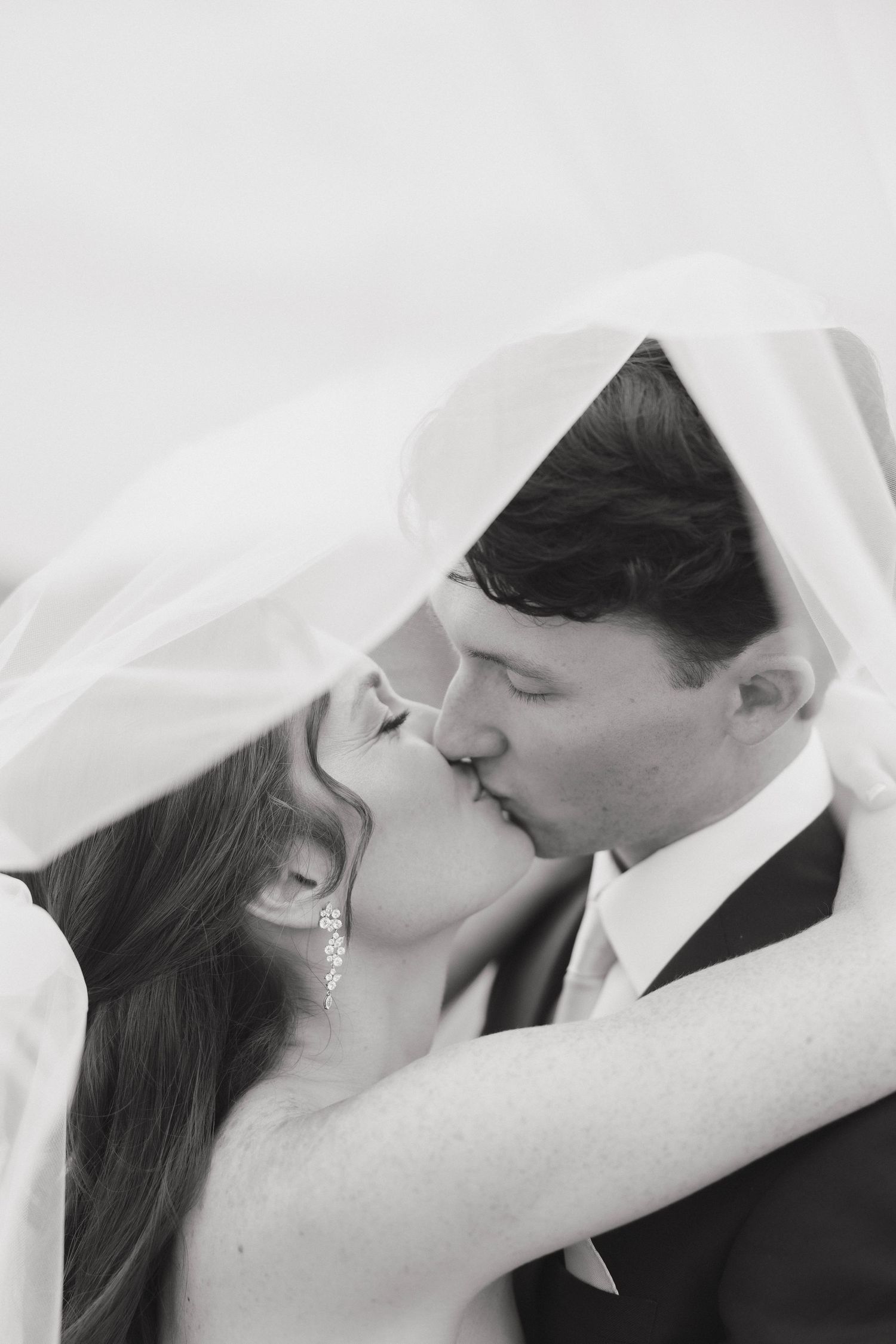 Romantic black and white wedding photos capture tender moments between bride and groom under flowing veil.