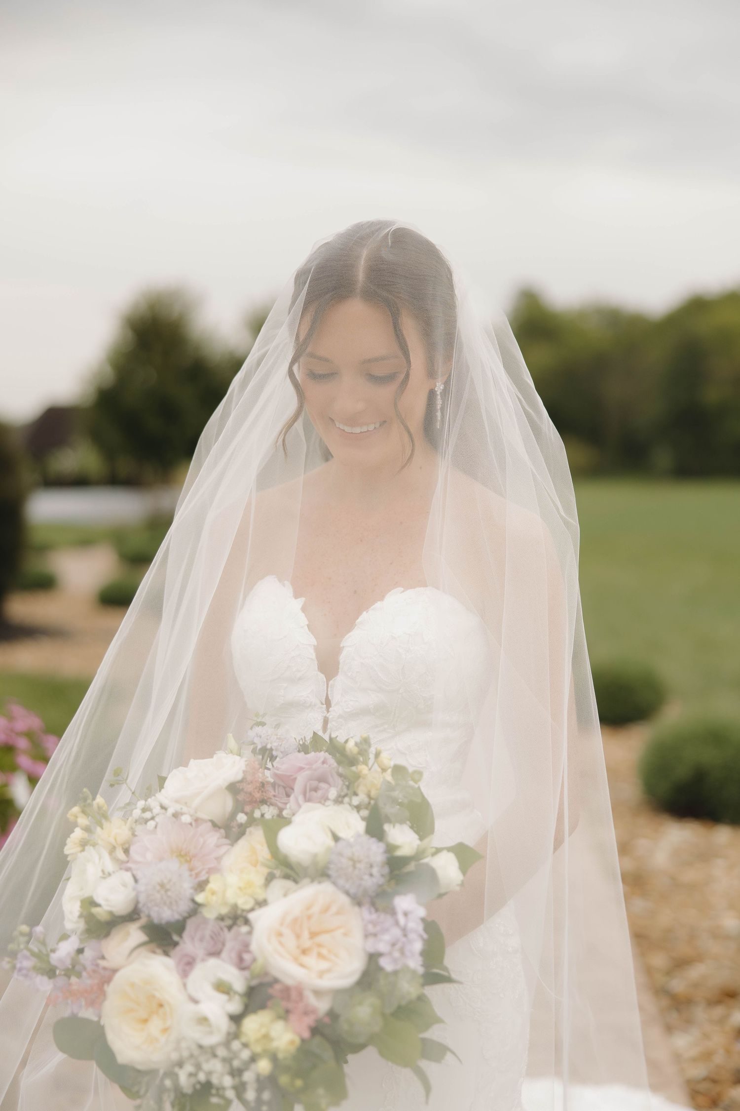 Delicate bridal bouquet featuring soft pink and white flowers with greenery against an outdoor background.
