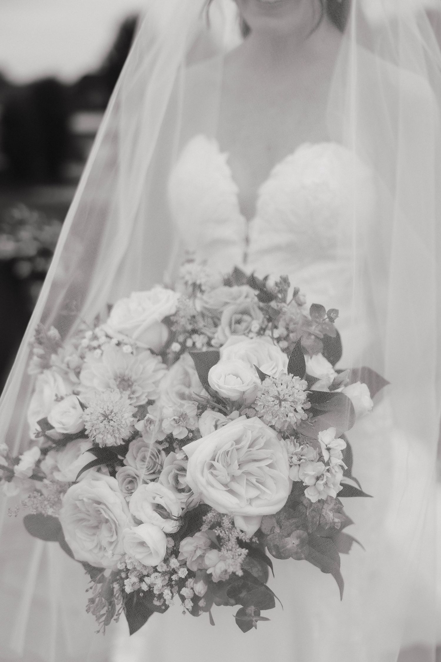 Delicate white and blush wedding bouquet with roses and mixed florals in soft black and white tones.