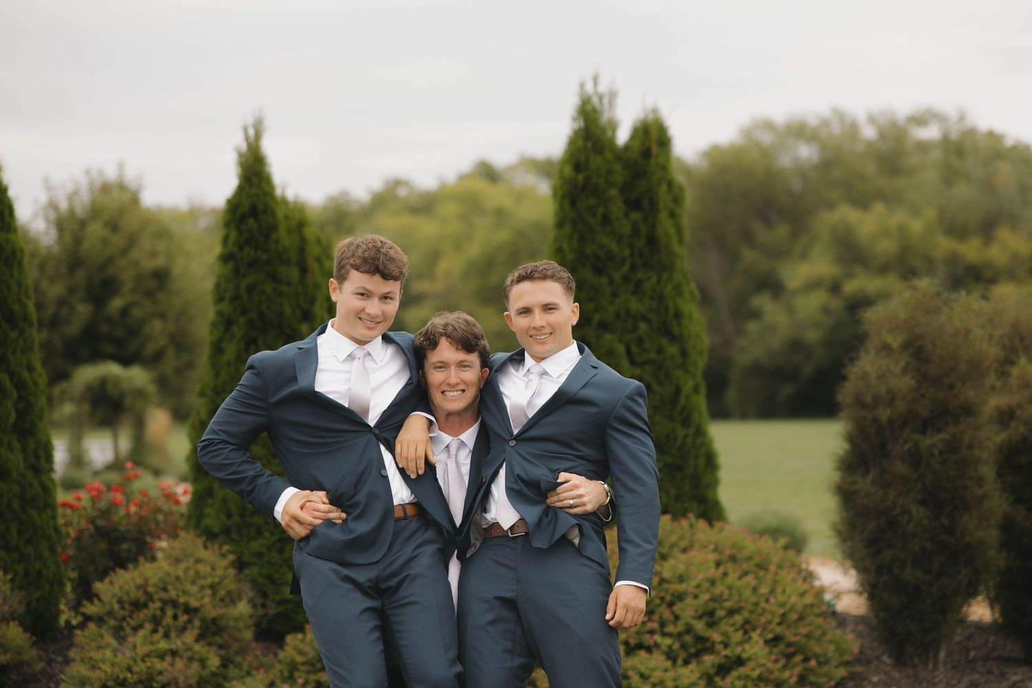 Groomsmen in navy suits pose together outdoors at a wedding venue.