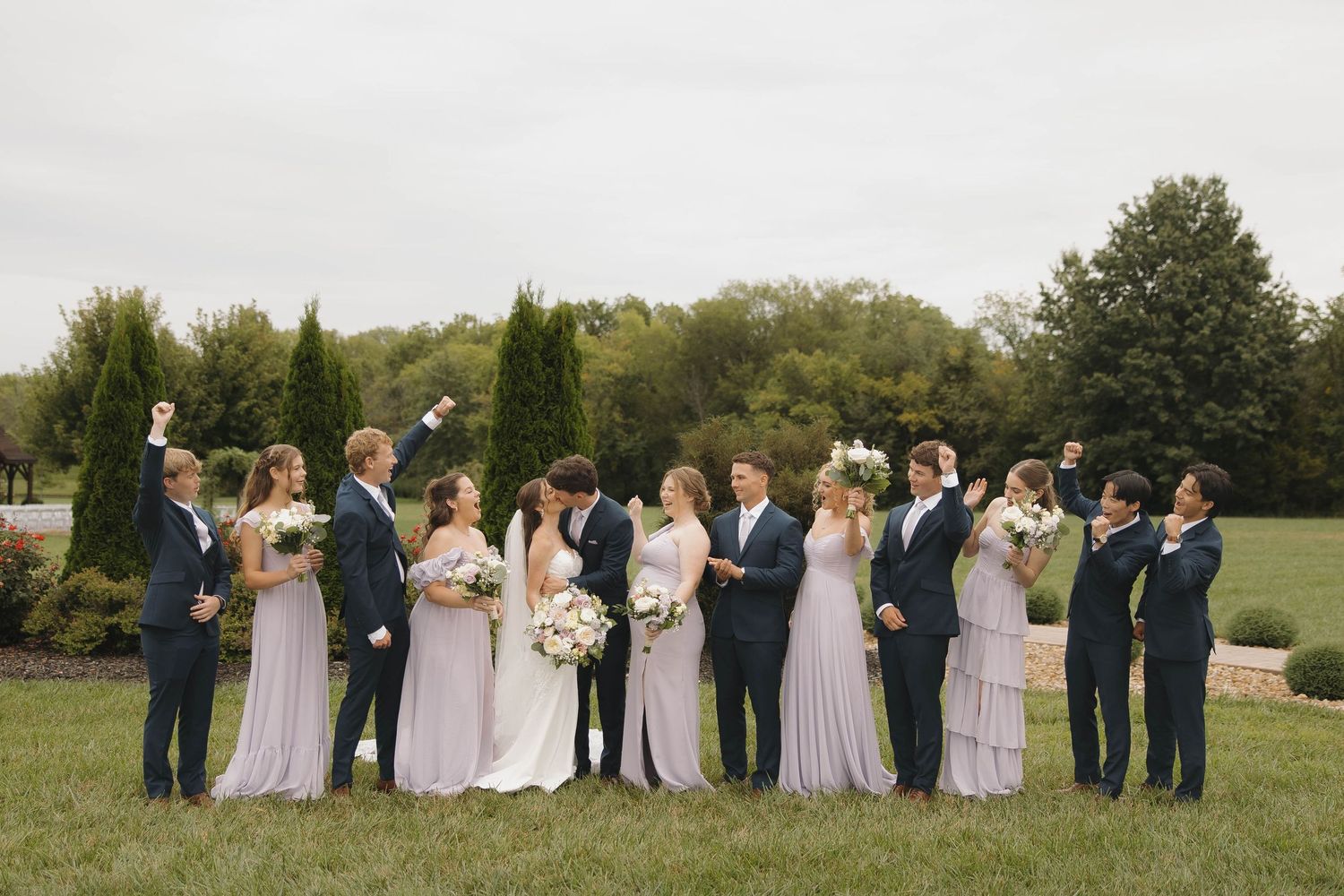 Wedding party members in navy and blush attire gather for formal group photos outdoors.