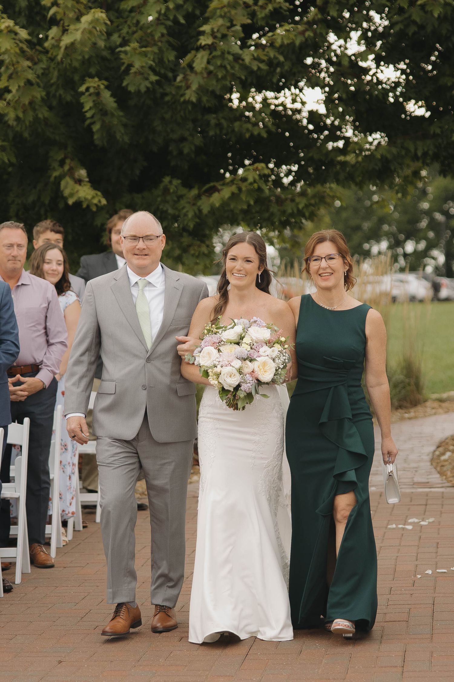 Wedding party members gather on a brick pathway during outdoor celebration.