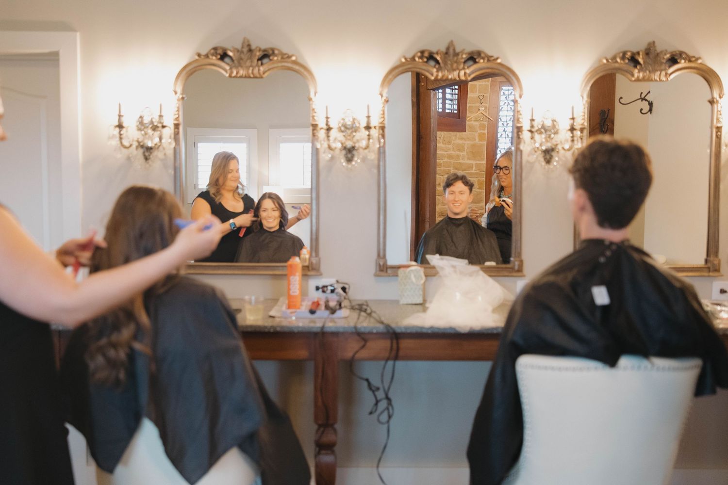 Hair stylist performs professional haircut service in an elegant salon with crystal chandeliers and ornate mirrors.