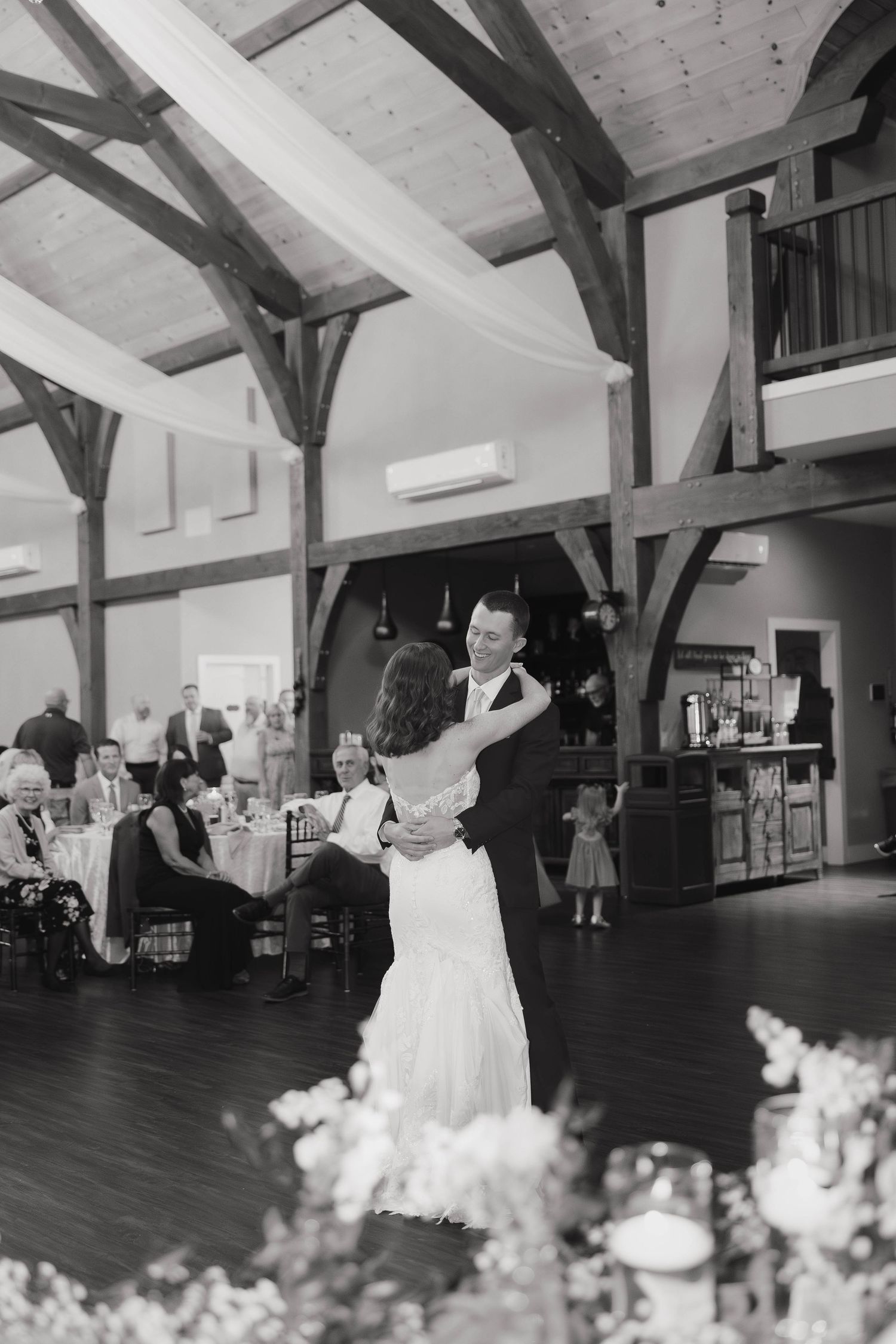 Couples dancing together in a rustic venue hall with exposed wooden beams on the ceiling during a celebration event.