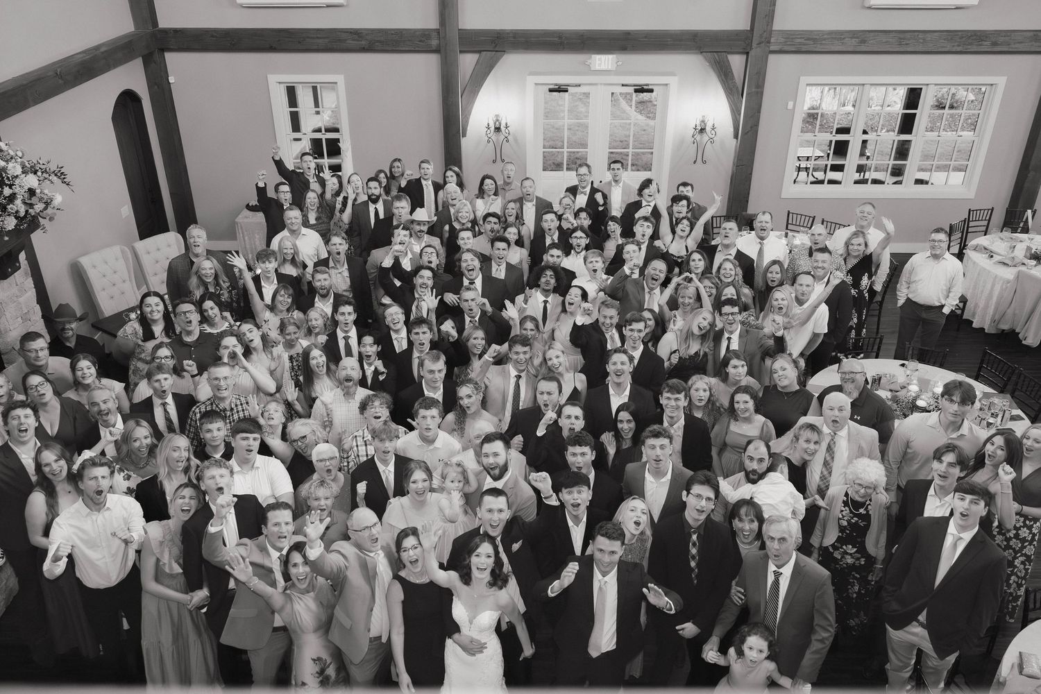 Large wedding reception crowd celebrating in an elegant white ballroom with crystal chandeliers.