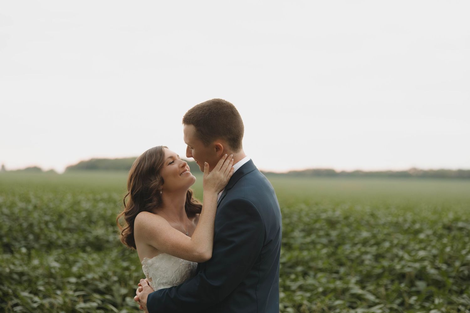 Newlyweds share an intimate moment in a pastoral field setting.
