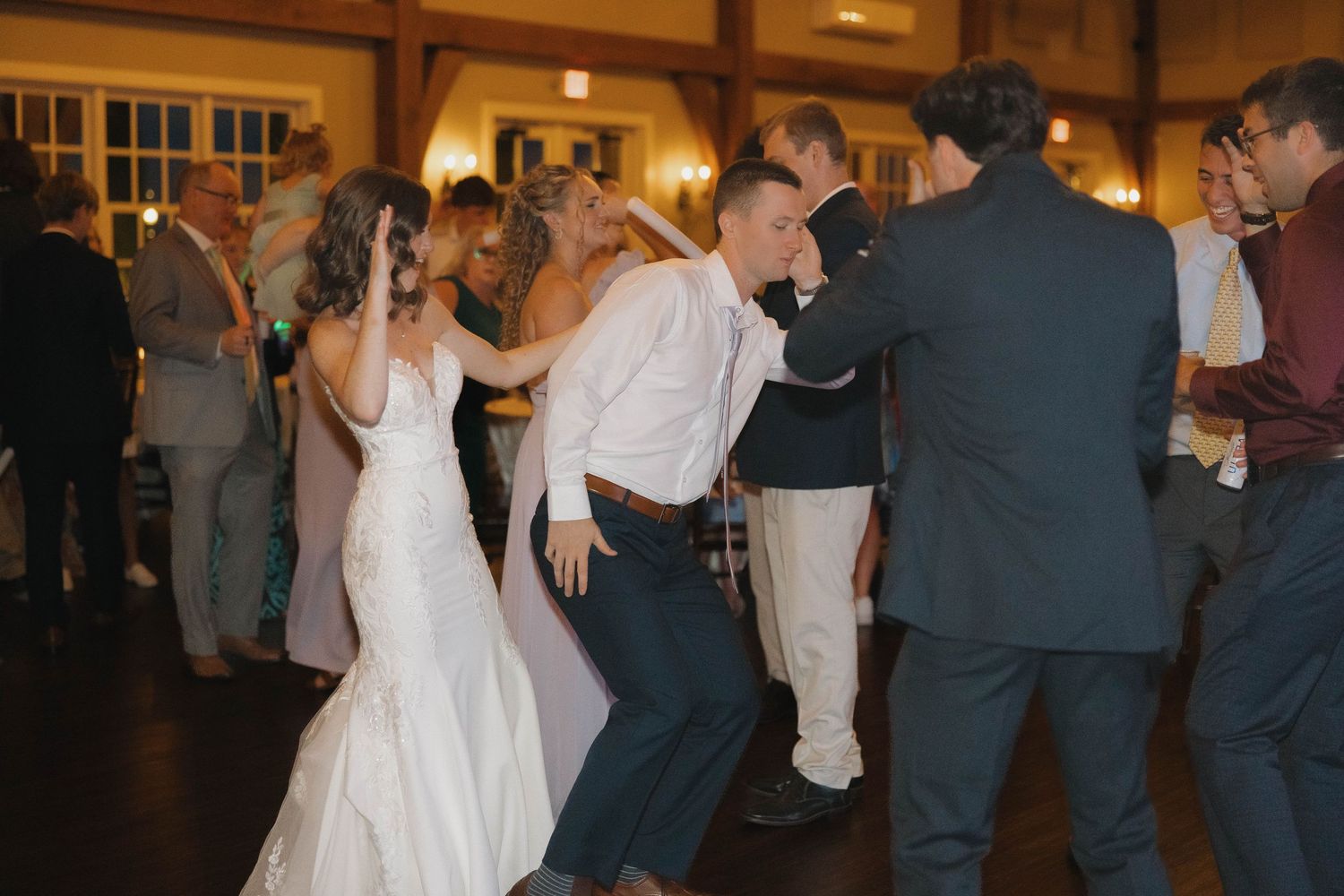 Wedding guests dance and celebrate on a warmly lit dance floor during an evening reception.
