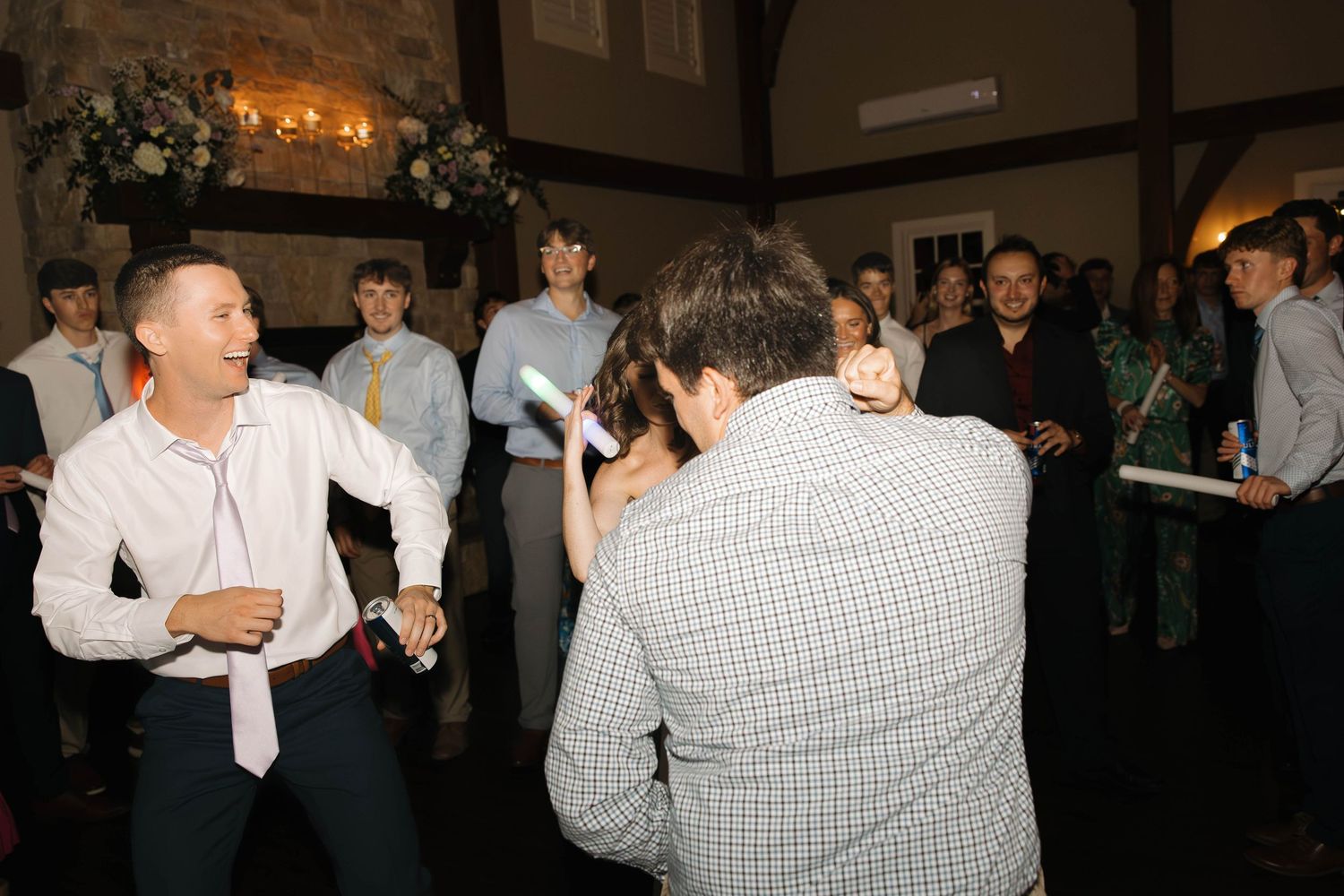 People dance and celebrate at a lively indoor social gathering with dim lighting.
