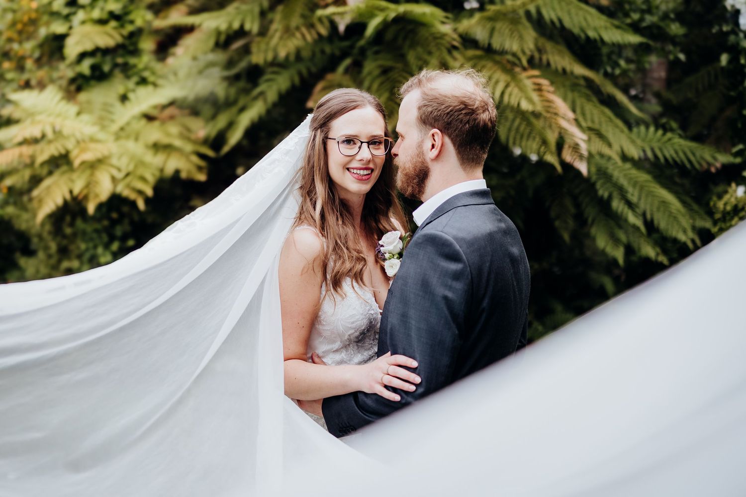 A couple in wedding attire poses in a sunlit garden during golden hour, creating a romantic and ethereal atmosphere.