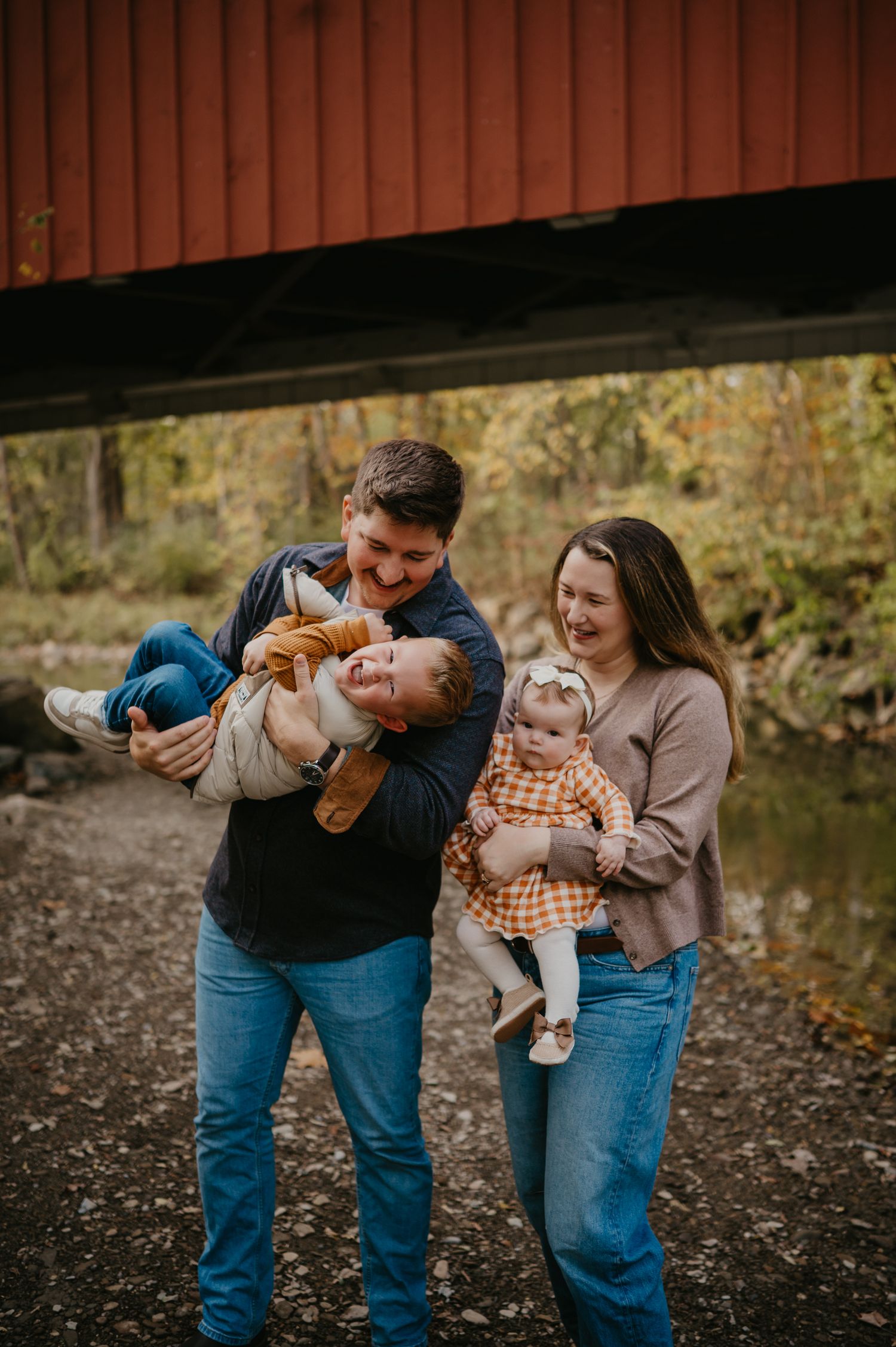 Couple with golden retriever dog posing inside a red covered bridge on a cloudy day.