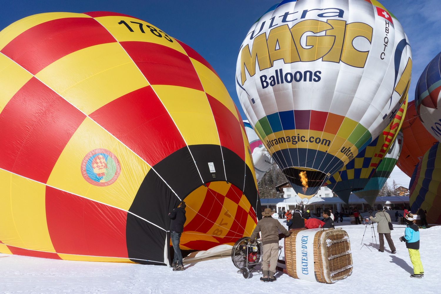 Colorful hot air balloons with red and yellow stripes line up across a blue sky during a festival launch event.