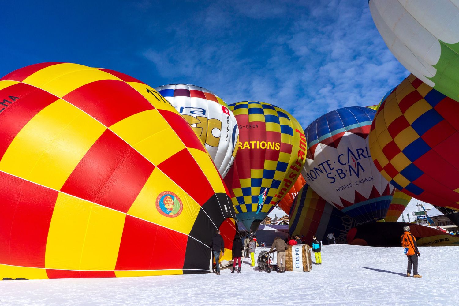 Colorful red and yellow parachutes dot the snowy mountain landscape against a bright blue winter sky.