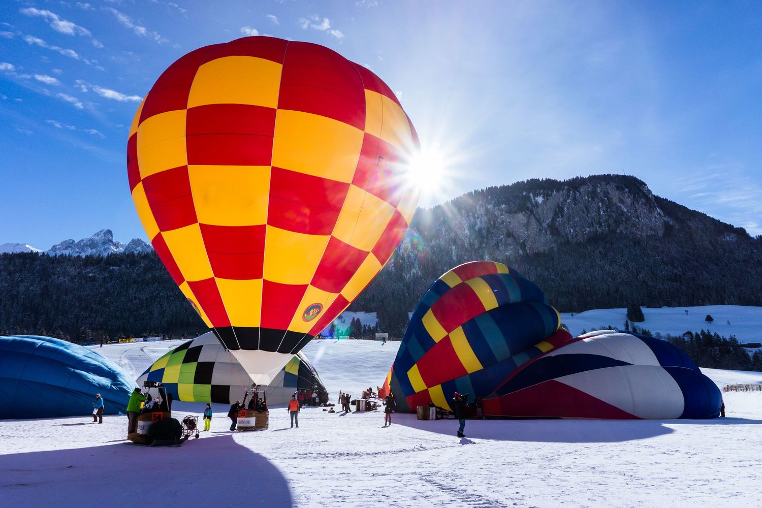 Colorful hot air balloons inflate against snowy mountain landscape during winter festival.