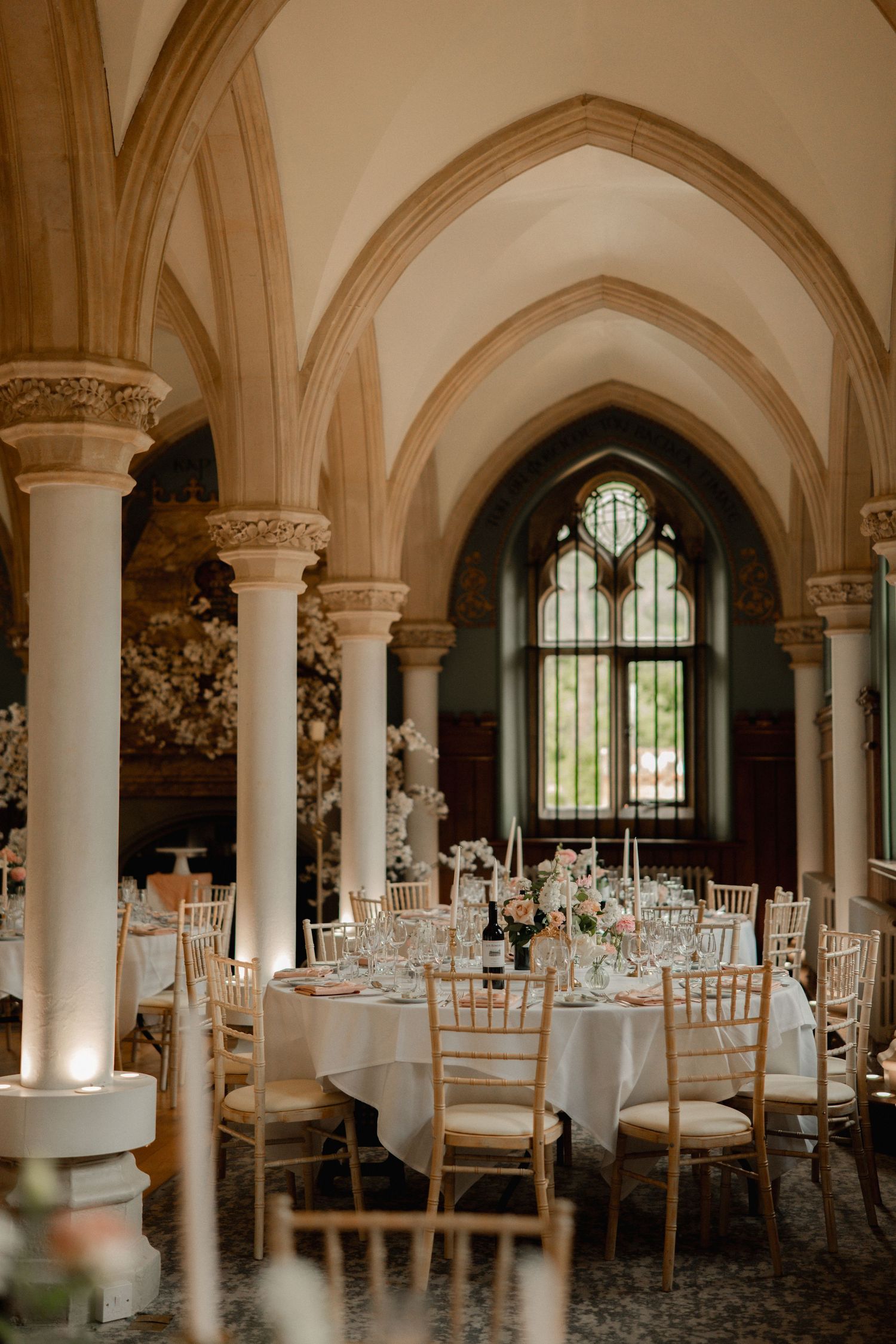 Elegant Gothic wedding reception hall with arched ceilings, gold chiavari chairs, and white floral centerpieces on round tables.