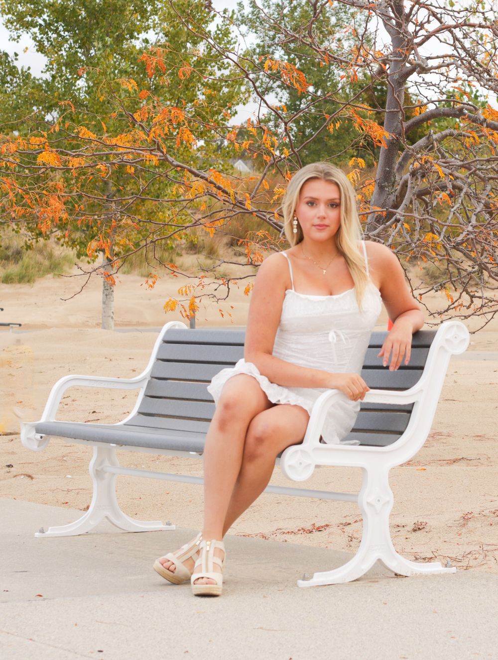 White summer dress ensemble on beach bench with autumn foliage in background.