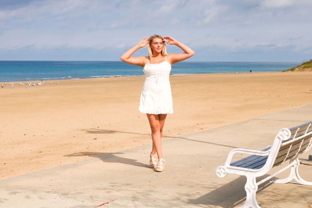 Person posing on sandy beach with bright blue ocean and sky in background.