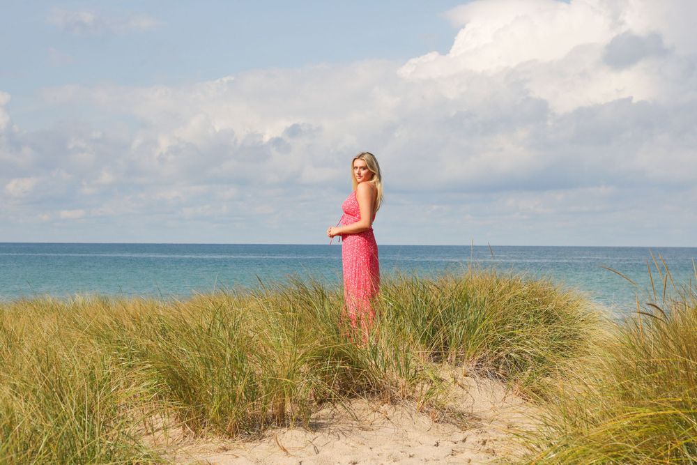 Figure standing on sand dune with beach grass and ocean horizon.